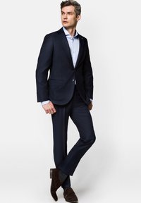 Granatowy garnitur z pojedynczym zapięciem, w zestawie z jasnoniebieską koszulą. Uzupełniony ciemnoskórzanymi zamszowymi butami i wzorzystymi skarpetkami.