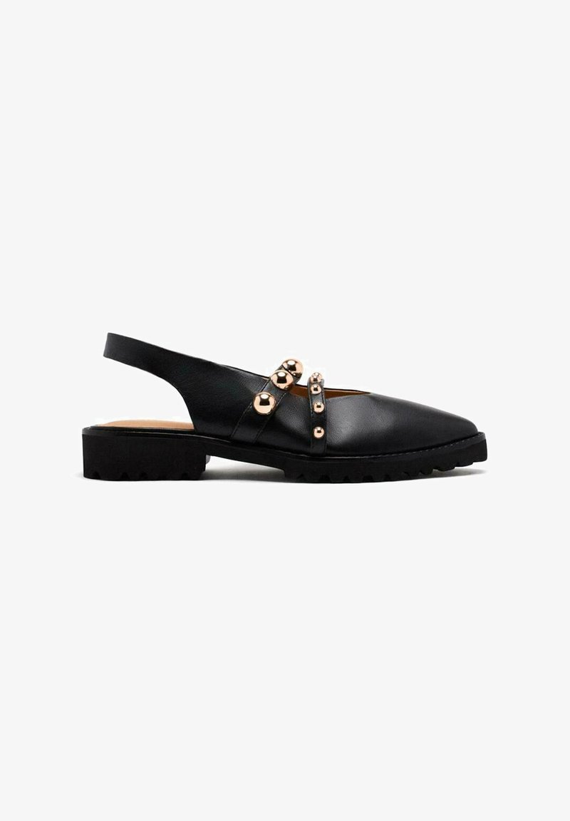 Zapato negro de piel tipo slingback con suela plana de goma, que presenta adornos metálicos en tono dorado y un diseño de punta afilada.