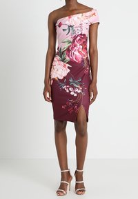 Robe florale décolletée, combinant des tissus rose et bordeaux, ornée de grands motifs floraux et d'une fente sur le côté, fabriquée en matière lisse.