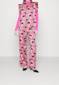 Růžový květinový souprava s volánovými rukávy a širokými kalhotami, doplněná lesklými černými podpatky.