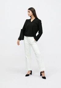 Melnā garroku blūze ar V-veida izgriezumu un brīvu piegriezumu. Kombinēta ar baltām taisnas piegriezuma biksēm, melniem augstiem papēžiem ar ieapaļu purngalu un melnu liela izmēra somu.