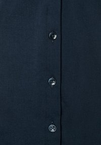 Dunkelblaue Hemd mit glatter Stofftextur, sechs Knöpfen in kontrastierenden Farbtönen und einem schlichten Design ohne Muster.