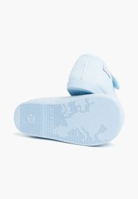 Zapatilla de tela azul claro con superficie texturizada, forma redondeada, suela flexible y un pequeño acento en forma de lazo en la parte trasera. Talla 25 impresa en la suela.