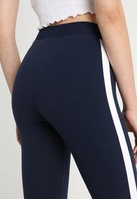 Leggings navy de tela elástica, con franjas laterales blancas, una cinturilla alta y una textura suave con forma ajustada.