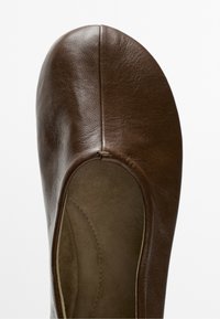 Close-up of a brown leather ballet flat shoe showing soft texture and rounded toe with minimal stitching on a white background.