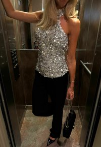 Top argentato con paillettes e scollatura halter, abbinato a pantaloni neri e tacchi a punta neri. Porta una borsa nera con dettagli dorati.