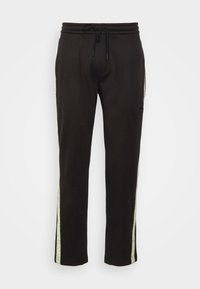 Melnas bikses sportam, izgatavotas no mīksta materiāla, ar regulējamu jostu un zaļām sānu svītrām, kurās ir "Calvin Klein Jeans" zīmola nosaukums.