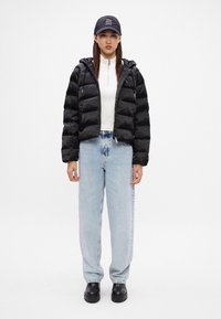 Czarna kurtka puchowa, zapinana z przodu, z kapturem, noszona na białej bluzie z długim rękawem; jasnoniebieskie luźne dżinsy; czarne masywne buty; czapka w kolorze czarnym.