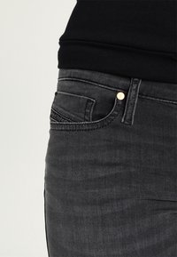 Närbild av en person som bär mörkgrå denimjeans med en liten framficka och en svart topp instoppad.