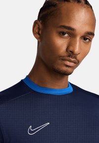 Maglietta sportiva navy con rifiniture del colletto blu, realizzata in un tessuto textured e con il logo Nike bianco sul petto. Maniche corte e vestibilità aderente.