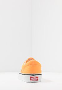 Oranžové plátěné nazouvací boty s bílou gumovou podrážkou, kontrastním černým lemem a červeným logem na patě. Hladký povrch, zaoblený design.