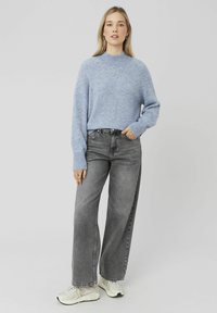 Pull en tricot bleu clair avec un col haut, associé à un jean gris à taille haute et à jambes larges, et des baskets blanches.