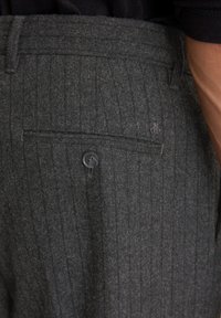 Grijze wolmix broek met een streeppatroon, een achterzak met een zwarte knop en subtiele logo-details nabij de zak.