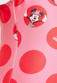 Roze zwemkledingstof met grote rode stippen en cirkelvormige afbeeldingen van een cartoonfiguur met een strik. Zachte textuur met gestikte naden.