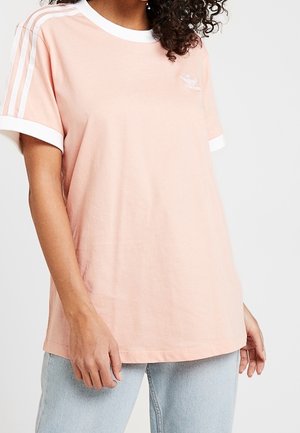 Helles rosa Baumwoll-T-Shirt mit weißen Akzenten an Kragen und Ärmeln. Verfügt über drei weiße Streifen auf den Schultern und ein kleines gesticktes Logo auf der Brust.