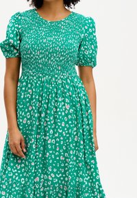 Grön klänning med leopardmönster, med puffärmar och smockad bodice. Flödande kjol med volangkant. Mjuk tygtextur.