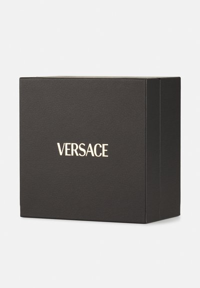 Fekete doboz, amelynek textúrája van, a frontján arany "VERSACE" logóval. Téglalap alakú, tiszta élekkel.