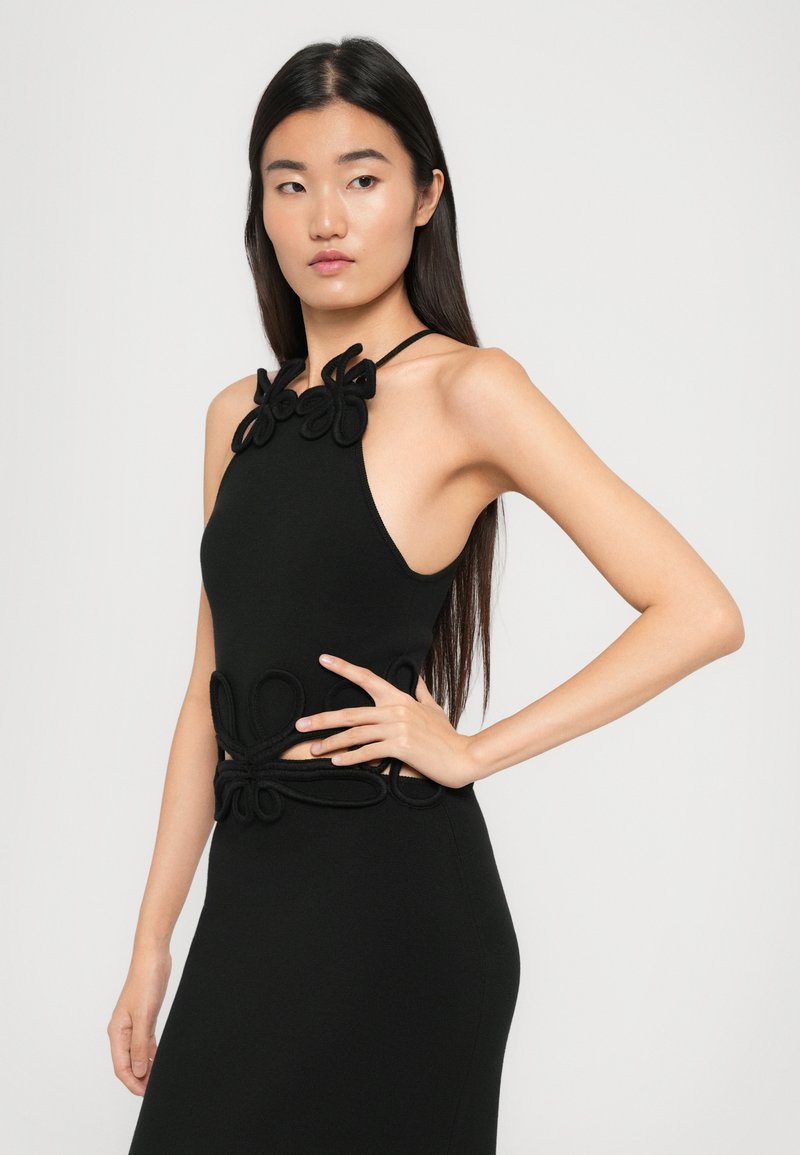 Robe noire à encolure dégagée mettant en avant des découpes au niveau de la taille, embellie de détails en tissu en boucle au niveau de l'encolure et de l'ourlet.
