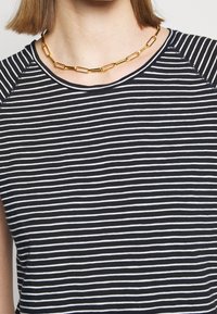 Randig svart- och vit T-shirt med rund halsringning och korta ärmar, med en mjuk textur och ett lager av guldhalsband.