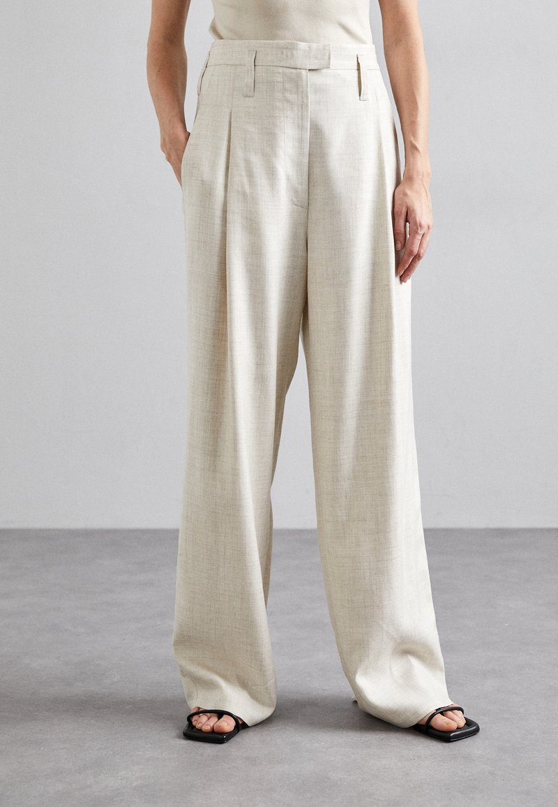 Ανοιχτό μπεζ παντελόνι ψηλής μέσης με πτυχώσεις, φαρδιά γραμμή, υφασμάτινη υφή και πλαϊνές τσέπες. Συνδυάζεται με μαύρες σανδάλια.
