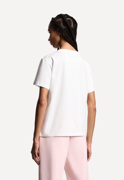 T-shirt bianca in cotone con vestibilità comoda, maniche corte e scollo rotondo classico, indossata con pantaloni rosa chiaro. Design semplice e versatile.