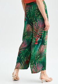 Pantaloni ampi verde con un motivo a foglia tropicale in varie tonalità di verde, rosa e accenni di rosso. Vita elastica, tessuto leggero.