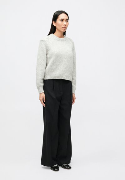 Svetlosivý pletený sveter s okrúhlym výstrihom a rebrovaným lemom, skombinovaný s vysoko pásovými čiernymi nohavicami s pásikmi a čiernymi topánkami.