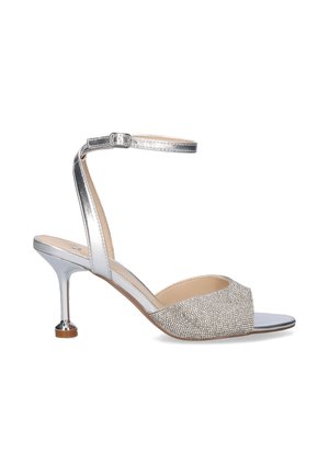 Sandalia plateada de tacón alto con correa en el tobillo y punta abierta, con una banda frontal texturizada y brillante y un tacón delgado y curvado.