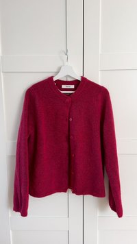 Cárdigan fucsia hecho de un material suave y texturizado, con un cuello redondo y seis botones de cierre, que cuenta con mangas largas y un ajuste relajado.