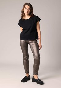 Zwarte top met korte mouwen, gecombineerd met smalle metallic bronzen broeken en zwarte veterschoenen. Gladde textuur met een eenvoudig ontwerp.