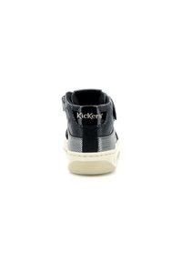 Zapatilla negra de media altura con cuero texturizado, un talón brillante y suela blanca en contraste. Presenta una correa de velcro y un logo grabado en la parte trasera.