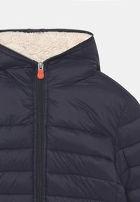 Mørkeblå dunjakke med hætte, der har en lynlåslukning fortil og en let, blød fleece-foring. Den har horisontale stikninger og en orange lynlås træk.