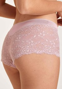 Roze heupbroek met kantafwerking van een gladde stof; bloemmotief van kant langs de onderrand; zachte textuur.