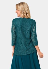 Top in pizzo teal con maniche a tre quarti, texture a motivo intricato e vestibilità ampia, abbinato a una gonna coordinata.