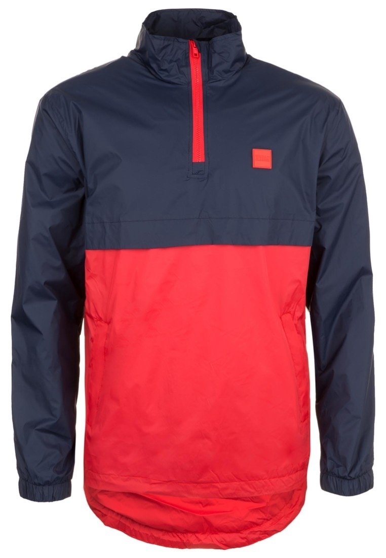 Windbreaker jacket featuring a half-zip design, navy blue upper section, bright red lower section, and elastic cuffs with a square logo patch.