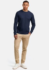 Marineblauwe geribbelde trui met lange mouwen en contrasterende kraag, gecombineerd met beige slim-fit chino's en witte sneakers, getoond van taille tot boven.