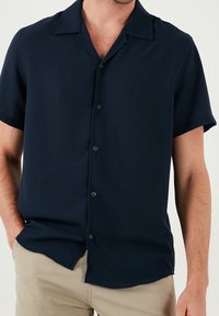 Ciemnogranatowa koszula z krótkim rękawem wykonana z gładkiej tkaniny, z kołnierzykiem typu camp, płaskimi guzikami i lekko luźnym krojem. Delikatna tekstura z połyskiem.
