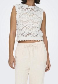 White knitted crop top with a hexagonal pattern, scalloped edges, and no sleeves, paired with light beige, drawstring linen pants.