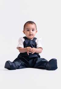 Navy blue waterproof overall with adjustable straps, a smooth texture, and a relaxed fit. Paired with a white shirt underneath.