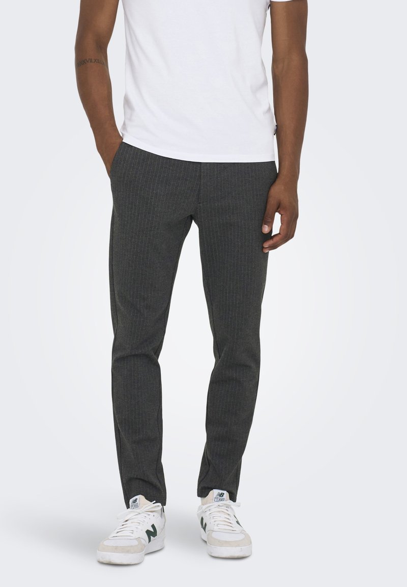 Pantalones oscuros a rayas con un corte slim, hechos de material texturizado, llevados con una camiseta blanca y zapatillas blancas.