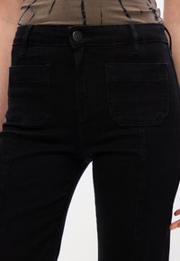 Čierne džínsy z denimu so stredne vysokým pásom, prednými vreckami a hladkou textúrou. Obsahujú kovové zapínanie a decentné švy.