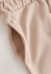 Bézs színű szövetnadrág rugalmas derékpánttal és a varrásba szőtt, jól látható oldalzsebbel.