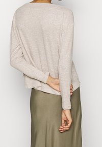 Pull beige en tricot texturé avec une coupe décontractée et un large col, superposé sur une jupe vert olive, affichant un look simple et décontracté.
