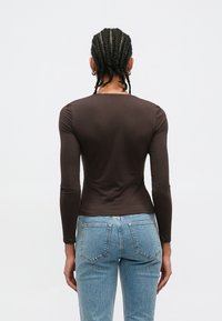 Haut marron à manches longues ajusté avec un col rond, associé à un jean denim bleu clair avec poches arrière et une légère élasticité.