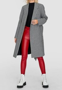 Zwart-wit houndstooth lange jas over een aansluitend zwart topje, gecombineerd met glanzende rode leren leggings en witte veterschoenen voor in de strijd.