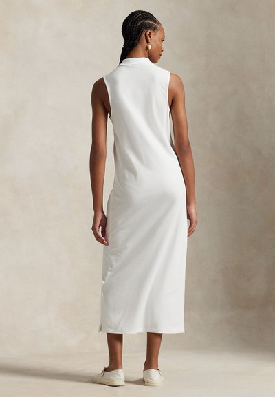 Biała sukienka bez rękawów z kołnierzykiem, o prostym kroju z bocznymi rozcięciami, wykonana z miękkiego materiału, w połączeniu z białymi, casualowymi butami.