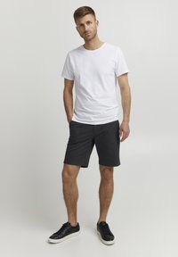 T-shirt en coton blanc associé à un short gris. Le short a une texture lisse et une taille élastique. Baskets noires au design simple.
