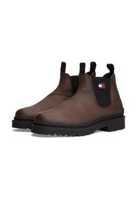 Botas Chelsea de cuero marrón con paneles elásticos negros a los lados, lengüetas, suelas de goma negra gruesa, y el logo de Tommy Jeans en el panel lateral.