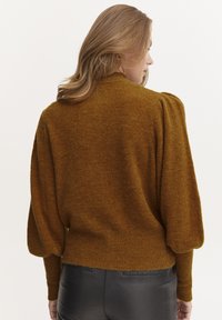 Maglione marrone con texture, collo alto, maniche a sbuffo e orlo a coste, abbinato a pantaloni di pelle nera.