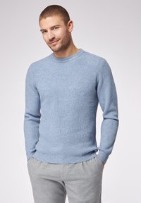 Maglione azzurro chiaro a coste con scollatura a girocollo e maniche lunghe, abbinato a pantaloni a quadri grigi. Tessuto morbido, design aderente.